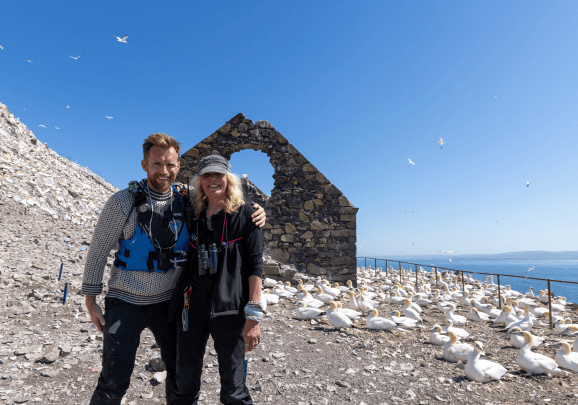 Auf der Felseninseln Bass Rock stehen der Expeditionsleiter und ein Gast der Kreuzfahrt vor einer Vogelkolonie Basstölpel